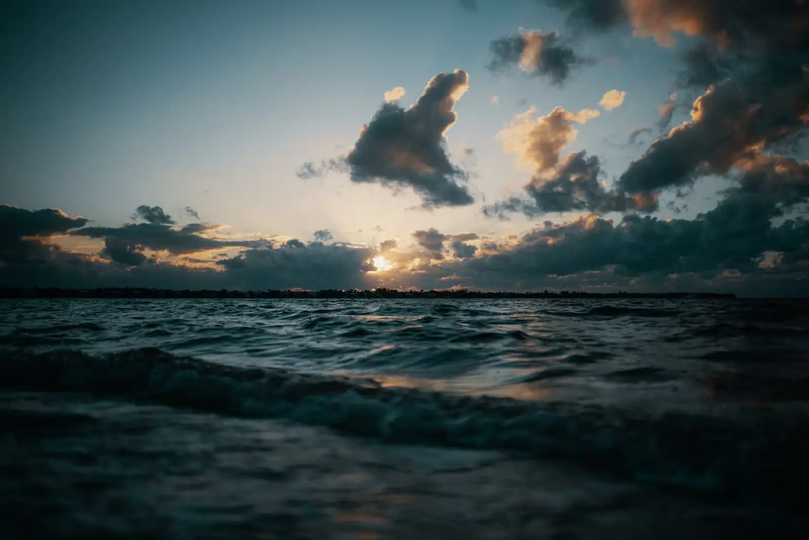 A low sun breaking through broken cloud over choppy water, photographed from just above the surface