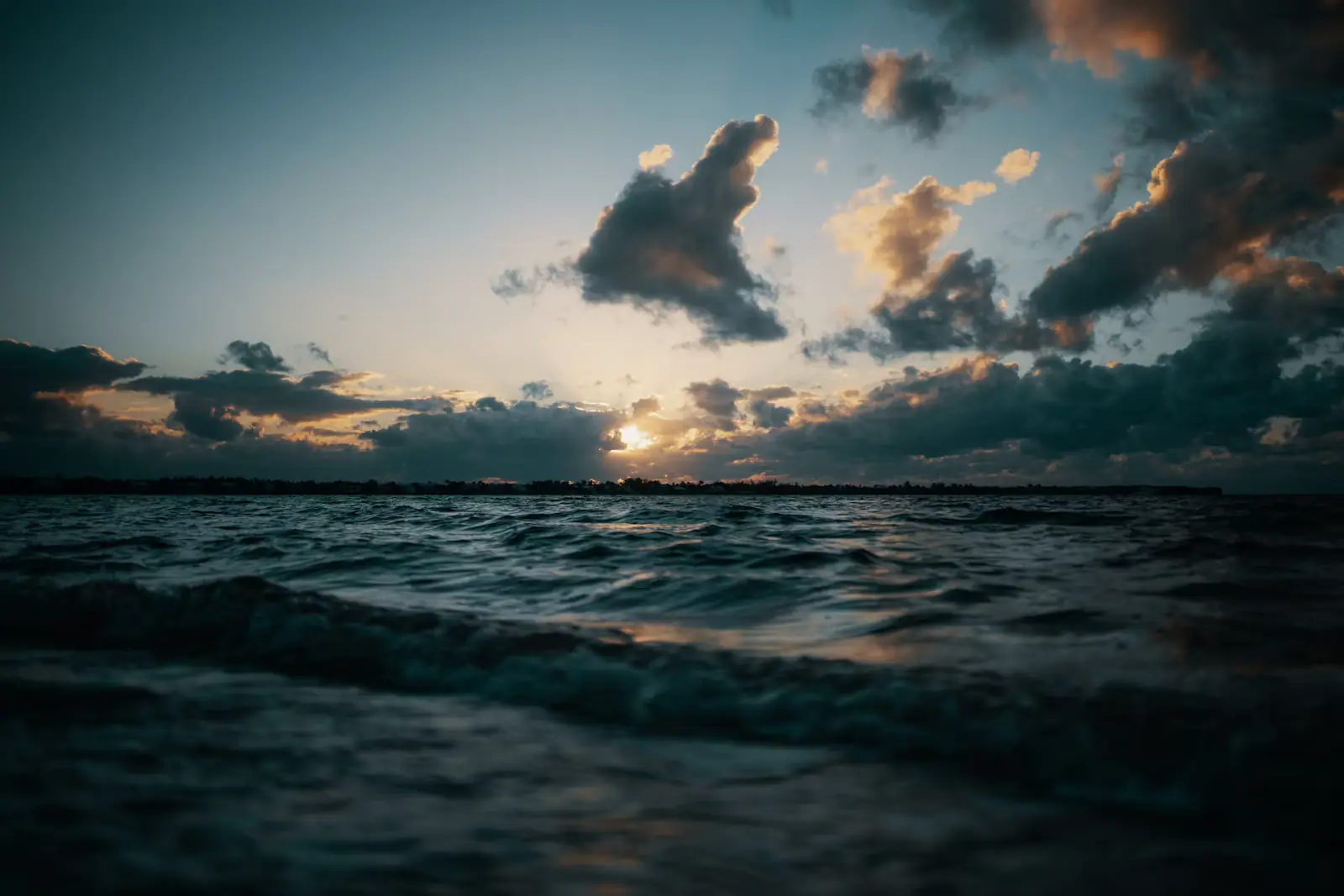 A low sun breaking through broken cloud over choppy water, photographed from just above the surface
