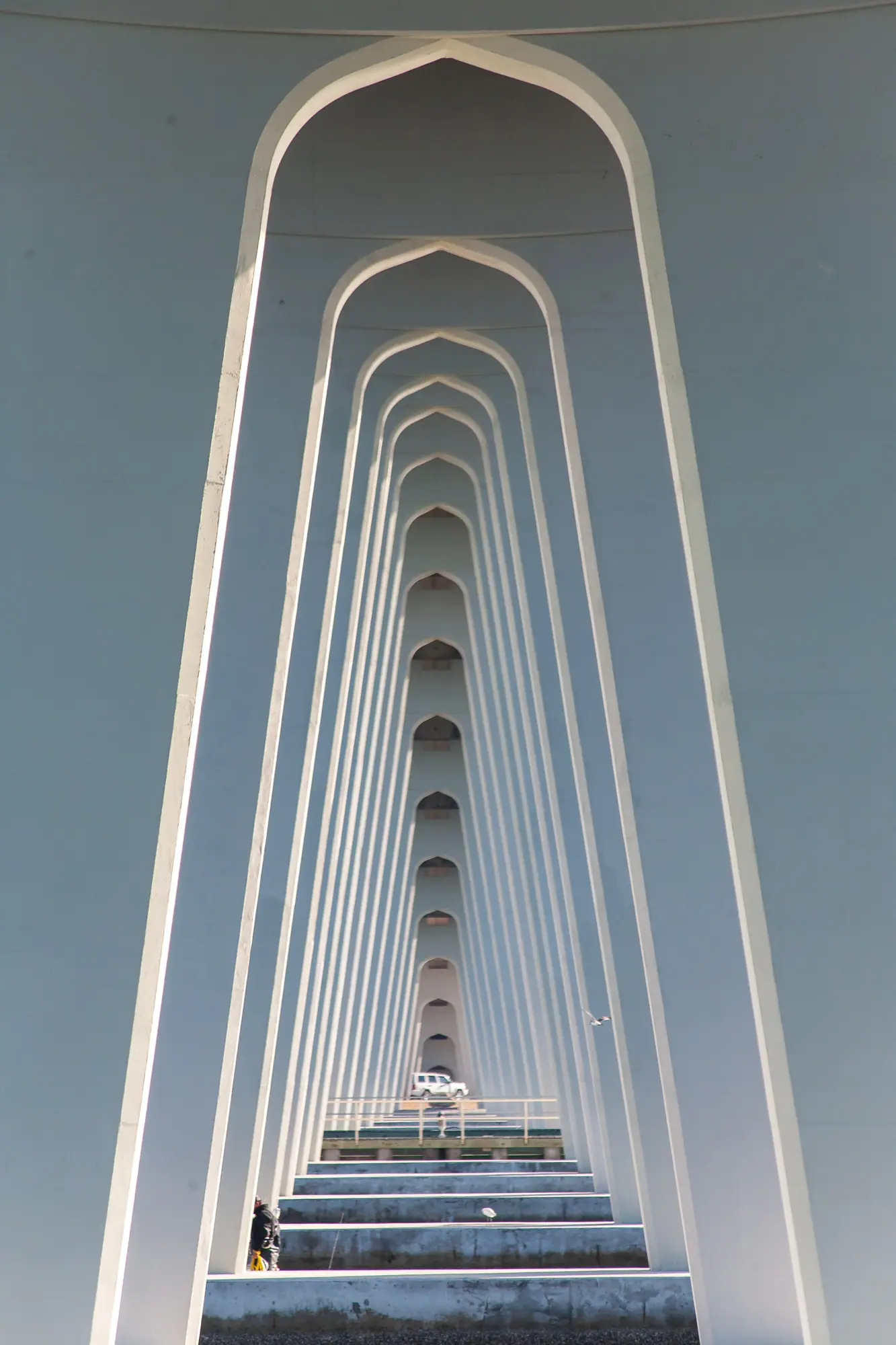 A long fixed highway bridge arcing over a wide tidal river under a pale sky